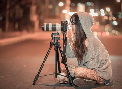Girl photographing with long lens DSLR and tripod at night
